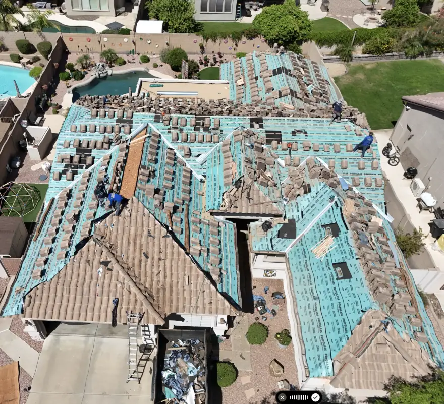 Tile roof during underlayment replacement, with tiles stacked above the exposed new underlayment.
